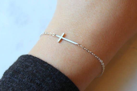 Silver bracelet with a cross on a wrist against a light background