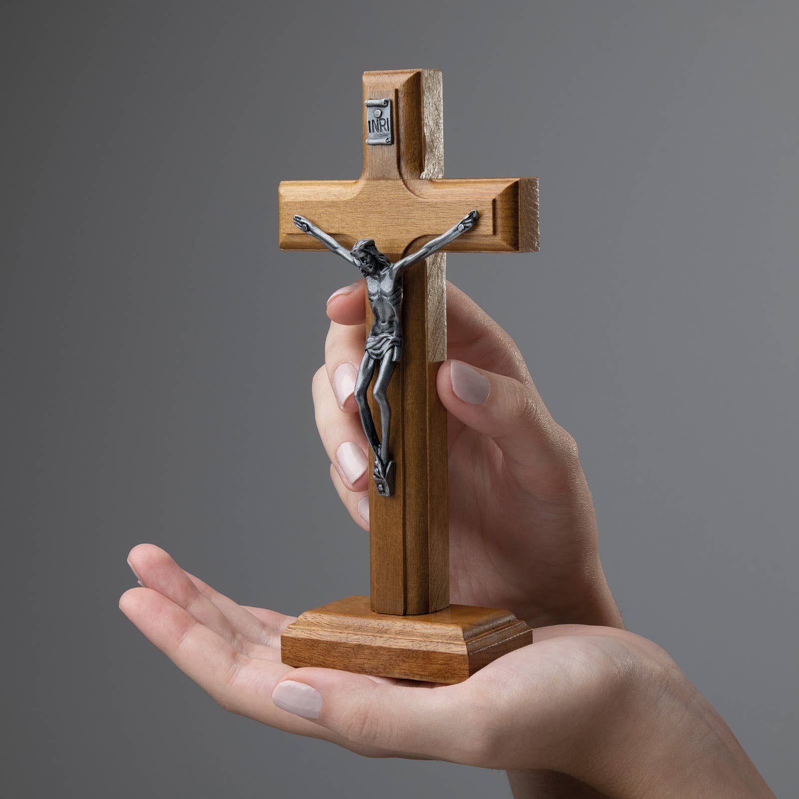 Wooden cross with a silver figure of Jesus  held in a hand against a gray background