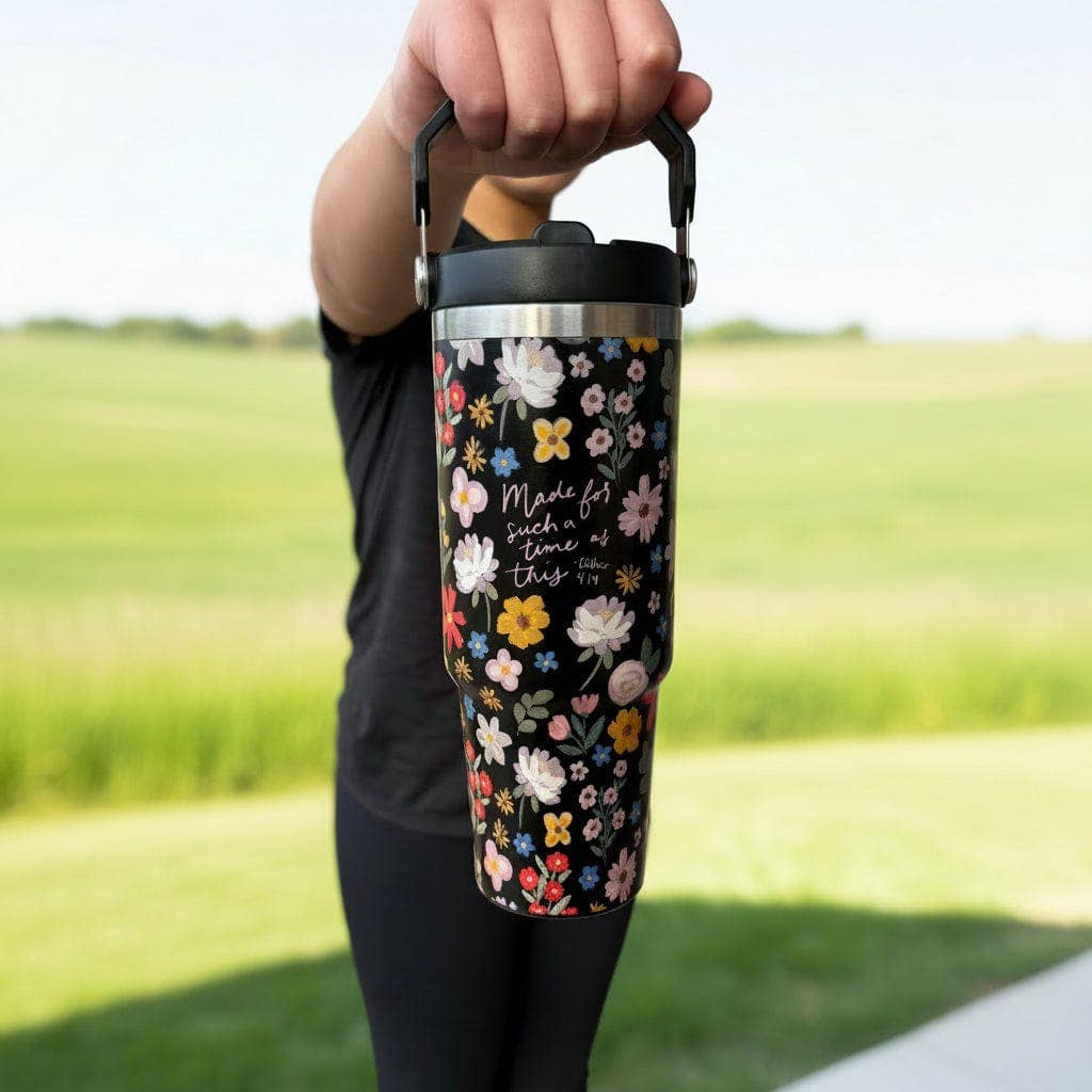 Person holding a floral-patterned insulated tumbler outdoors with a green field background