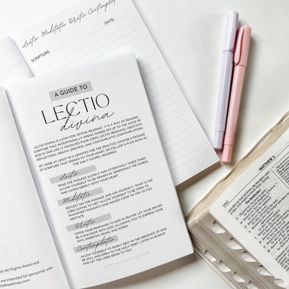 Open book with 'A Guide to Lectio Divina' text and two pens on a white surface