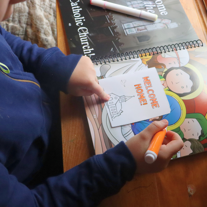 Child coloring a card with 'Welcome Home!' text on a table with educational materials.