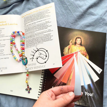 Color swatch card held over a book with a colorful rosary and religious text.