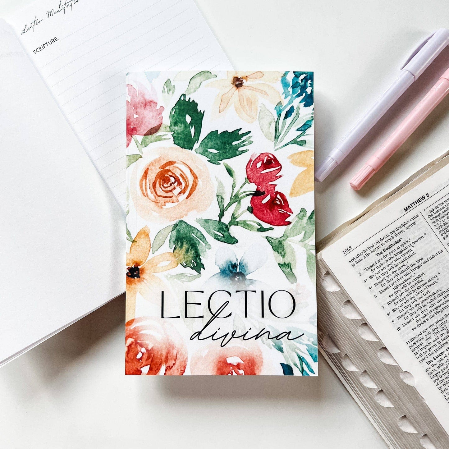 Floral notebook with 'Lectio divina' text on a white surface with stationery items.
