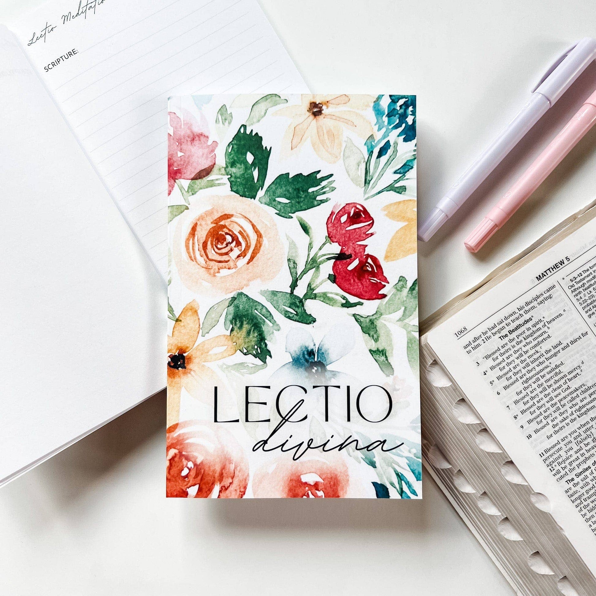 Floral notebook with 'Lectio divina' text on a white surface with stationery items.