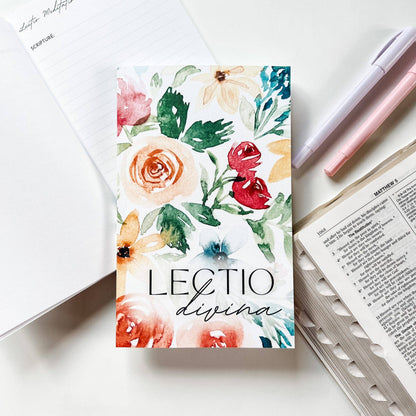 Floral notebook with 'Lectio divina' text on a white surface with stationery items.